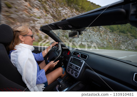 Young woman driving convertible along scenic ocean coast and mountain road at sunset, carefree summer vacation, travel freedom and adventure on coastal highway Young woman driving convertible along scenic ocean coast and mountain road at sunset, carefree summer vacation, travel freedom and adventure on coastal highway 133910481