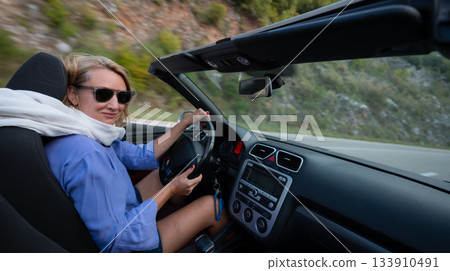 Young woman driving convertible along scenic ocean coast and mountain road at sunset, carefree summer vacation, travel freedom and adventure on coastal highway Young woman driving convertible along scenic ocean coast and mountain road at sunset, carefree summer vacation, travel freedom and adventure on coastal highway 133910491