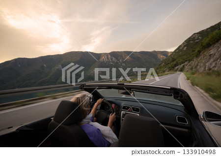Young woman driving convertible along scenic ocean coast and mountain road at sunset, carefree summer vacation, travel freedom and adventure on coastal highway Young woman driving convertible along scenic ocean coast and mountain road at sunset, carefree summer vacation, travel freedom and adventure on coastal highway 133910498