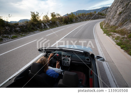 Young woman driving convertible along scenic ocean coast and mountain road at sunset, carefree summer vacation, travel freedom and adventure on coastal highway Young woman driving convertible along scenic ocean coast and mountain road at sunset, carefree summer vacation, travel freedom and adventure on coastal highway 133910508