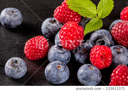 Macro photo of fresh ripe raspberries and blueberries on dark background Macro photo of fresh ripe raspberries and blueberries on dark background 133911371