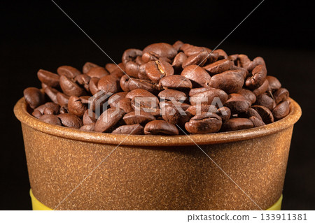 A plastic cup filled with fresh roasted coffee beans on a table A plastic cup filled with fresh roasted coffee beans on a table 133911381