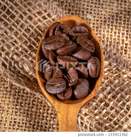 Beautiful wooden spoon displaying glossy coffee beans in detail 133911382