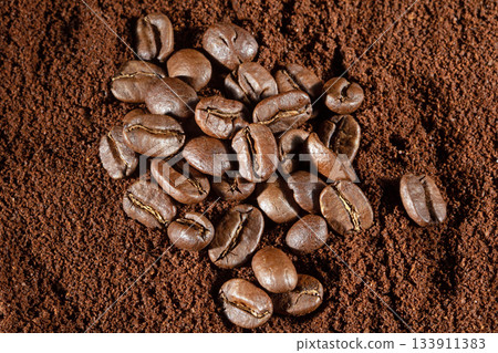 Top view of scattered coffee beans on a background of ground coffee Top view of scattered coffee beans on a background of ground coffee 133911383