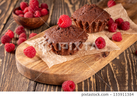 Gourmet chocolate muffins topped with fresh raspberries for a tasty delight 133911384