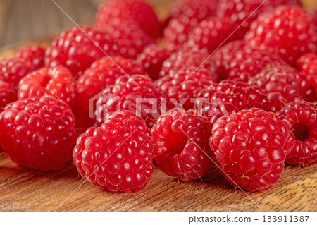 Close-up of fresh ripe raspberries scattered on a rustic table surface Close-up of fresh ripe raspberries scattered on a rustic table surface 133911387