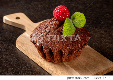 Close-up of a decorated raspberry muffin on a wooden cutting board Close-up of a decorated raspberry muffin on a wooden cutting board 133911398