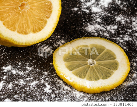 Fresh sliced lemon and a sprinkle of powdered sugar on black surface Fresh sliced lemon and a sprinkle of powdered sugar on black surface 133911405