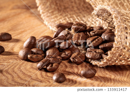 Close-up of coffee beans spilling from a jute bag onto a table surface 133911417
