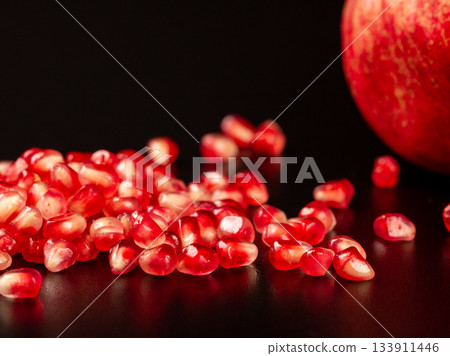 Close-up of pomegranate fruit with vibrant seeds on black background Close-up of pomegranate fruit with vibrant seeds on black background 133911446