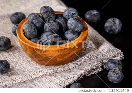 A wooden bowl overflowing with juicy blueberries on a soft linen napkin 133911449