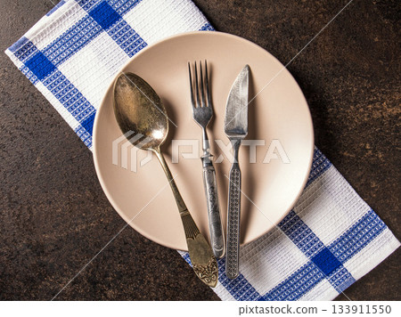 Elegant flat lay of vintage cutlery and plate on checkered napkin 133911550