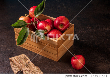 A rustic wooden box on a black table surrounded by ripe red apples 133911561