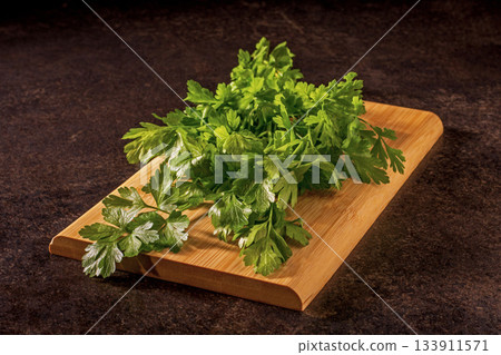 Fresh bunch of parsley on a rustic wooden kitchen cutting board Fresh bunch of parsley on a rustic wooden kitchen cutting board 133911571