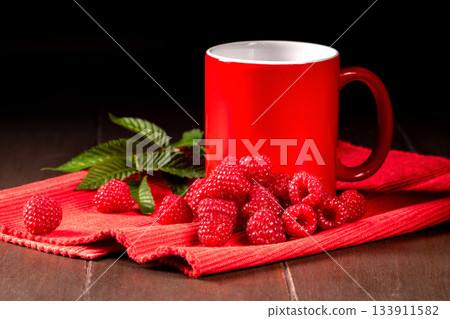 A vibrant red tea mug surrounded by fresh, ripe raspberry berries A vibrant red tea mug surrounded by fresh, ripe raspberry berries 133911582