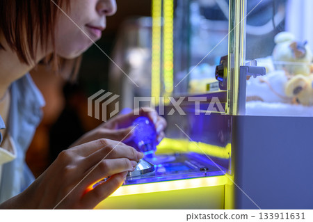 特寫鏡頭：一位年輕女子全神貫注地玩著抓娃娃機 133911631