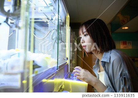 一位女士在渡輪上的遊戲中心嘗試玩抓娃娃機。 一位女士在渡輪上的遊戲中心嘗試玩抓娃娃機。 133911635