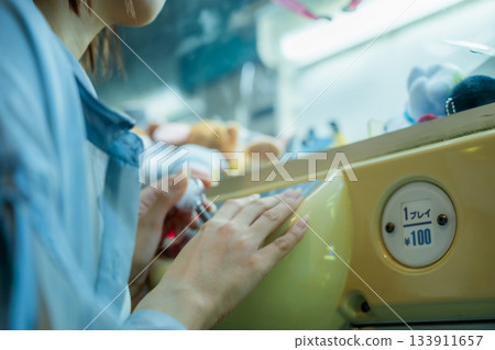 一位女士正在渡輪遊戲中心玩抓娃娃機,全神貫注。 一位女士正在渡輪遊戲中心玩抓娃娃機,全神貫注。 133911657