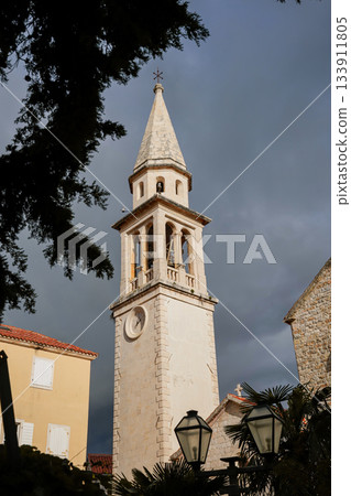 Photo taken from a low angle showing a church tower in the historic old town of Budva, Montenegro. Focus on medieval architecture, European heritage, and iconic city landmarks. Photo taken from a low angle showing a church tower in the historic old town of Budva, Montenegro. Focus on medieval architecture, European heritage, and iconic city landmarks. 133911805
