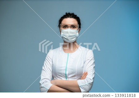 Female doctor in medical mask and protective glasses posing confidently in uniform Female doctor in medical mask and protective glasses posing confidently in uniform 133911818