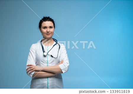 Female doctor with stethoscope standing confidently in white uniform on clean blue studio background 133911819