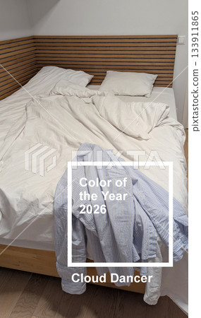 Vertical unmade bed with white bedding in cloud dancer color of the year 2026, blue striped shirt hanging on wooden bed, cozy real bedroom interior in neutral palette and soft lighting Vertical unmade bed with white bedding in cloud dancer color of the year 2026, blue striped shirt hanging on wooden bed, cozy real bedroom interior in neutral palette and soft lighting 133911865
