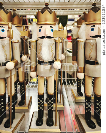 Row of wooden white and gold nutcracker kings with axes and crowns on retail shelf, bright festive mood 133911884