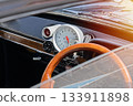 Close view of vintage car dashboard with wooden steering wheel, large analog tachometer and chrome details, warm sunlight flare 133911898