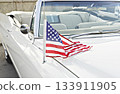 Small American flag mounted on antenna of white classic convertible, stars and stripes draped across hood in bright daylight, patriotic summer vibe 133911905