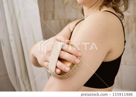 Woman performing dry brushing routine on her arm for skin care Woman performing dry brushing routine on her arm for skin care 133911986