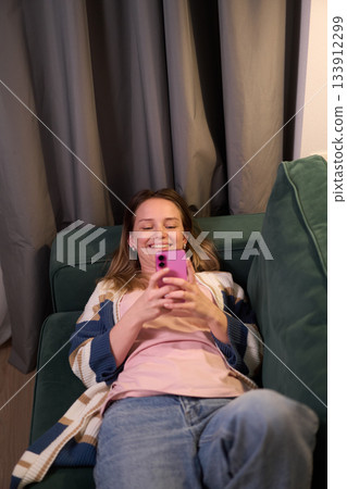 Woman lying on sofa using smartphone indoors 133912299