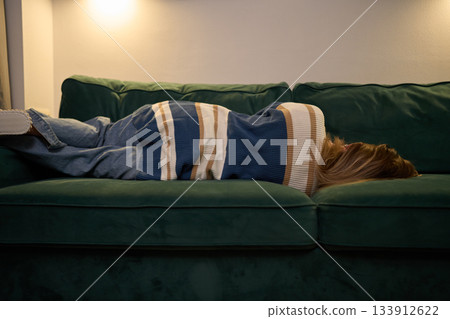 Cozy solitude with woman resting on sofa under soft evening light Cozy solitude with woman resting on sofa under soft evening light 133912622