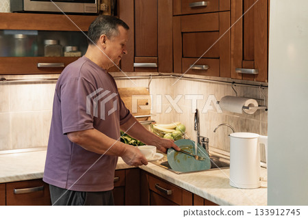 Adult man cleaning dishes in home kitchen, preparing for healthy breakfast. Morning routine with fresh ingredients and natural light. Morning Home Cooking Making and Eating Breakfast 133912745