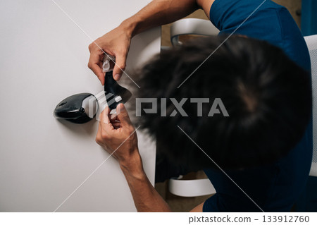 Close-up top view of technician male meticulously cleaning disassembled vertical mouse with disinfectant wipe sitting at white table, ensuring hygiene and optimal performance in professional setting Close-up top view of technician male meticulously cleaning disassembled vertical mouse with disinfectant wipe sitting at white table, ensuring hygiene and optimal performance in professional setting 133912760