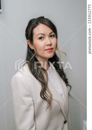 Front view of professional Asian businesswoman in cream blazer and white t-shirt looking at camera with confident smile, representing success, leadership, and professionalism. 133912775