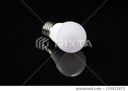Elegant white matte led bulb reflecting on a black mirrored surface Elegant white matte led bulb reflecting on a black mirrored surface 133912873