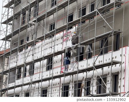Construction workers finishing facade on scaffolding. Industry, teamwork, and progress through detailed architectural craftsmanship. 133912902