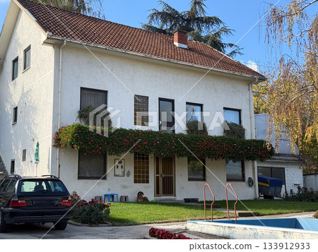 Suburban house with garden and red roof. Family life, comfort, and peaceful neighborhood atmosphere symbolizing home warmth and stability. 133912933