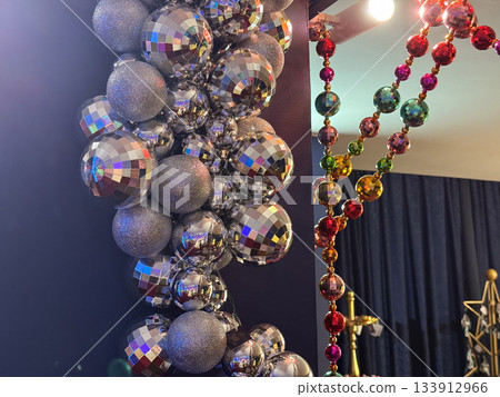 Christmas Silver disco ornaments and glitter baubles forming festive column beside colorful bead garlands. Holiday glamour, party sparkle, holidays decoration brightness and vibrant seasonal charm. 133912966