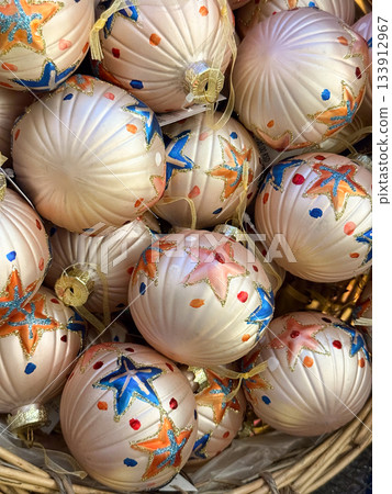 Basket filled with cream Christmas baubles painted with glitter stars and bright dots. Holiday craft, winter ornamentation, handmade festive charm and decorative gift appeal. 133912967