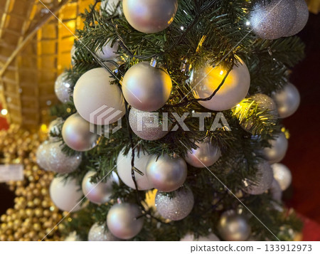 Christmas tree with frosted white and silver baubles glowing with warm lights. Winter elegance, peaceful holiday decoration, cozy festive atmosphere and seasonal charm. Christmas tree with frosted white and silver baubles glowing with warm lights. Winter elegance, peaceful holiday decoration, cozy festive atmosphere and seasonal charm. 133912973