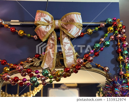 Velvet bow with golden trim among colorful Christmas bead garlands on festive decor. Holiday glamour, joyful winter brightness, celebration sparkle and decorative seasonal charm. Velvet bow with golden trim among colorful Christmas bead garlands on festive decor. Holiday glamour, joyful winter brightness, celebration sparkle and decorative seasonal charm. 133912974