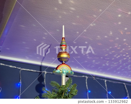 Colorful Christmas tree topper with shimmering projection on ceiling in soft light. Seasonal magic, winter celebration fantasy, joyful home spirit and festive ambience. Colorful Christmas tree topper with shimmering projection on ceiling in soft light. Seasonal magic, winter celebration fantasy, joyful home spirit and festive ambience. 133912982