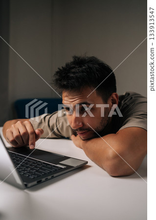 Vertical portrait of tired freelancer male leaning over laptop, deeply concentrating on critical project, displaying professional determination and work ethic. Concept of remote workplace. 133913547