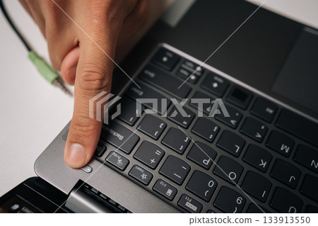 Close-up view of male finger pressing power button on laptop keyboard sitting at table, initiating journey of productivity or gaming excitement in modern workspace. Concept of online entertainment. Close-up view of male finger pressing power button on laptop keyboard sitting at table, initiating journey of productivity or gaming excitement in modern workspace. Concept of online entertainment. 133913550