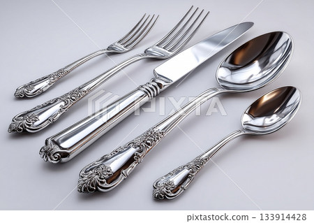 Emphasizing symmetry and elegance. Full silverware set. Including soup spoon, dinner fork, knife, dessert fork and teaspoon, perfectly arranged on a white background. Formal dining setting. 133914428