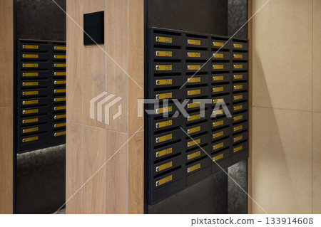 Neatly arranged mailboxes along corridor walls, Orderly line of mailboxes in city housing corridor, Well-organized row of mailboxes with brass plates in urban apartment hallway Neatly arranged mailboxes along corridor walls, Orderly line of mailboxes in city housing corridor, Well-organized row of mailboxes with brass plates in urban apartment hallway 133914608
