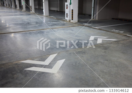 Brightly marked vehicle storage area, Concrete structure with guiding arrows and lighting, Industrial style subterranean garage with safety features and signage present 133914612