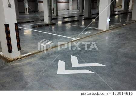 Brightly marked vehicle storage area, Concrete structure with guiding arrows and lighting, Industrial style subterranean garage with safety features and signage present 133914616