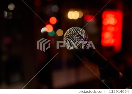 Performance setup with lighting and equipment, Closeup of microphone with vibrant stage illumination, Microphone prepared for performance amidst lively concert environment Performance setup with lighting and equipment, Closeup of microphone with vibrant stage illumination, Microphone prepared for performance amidst lively concert environment 133914664